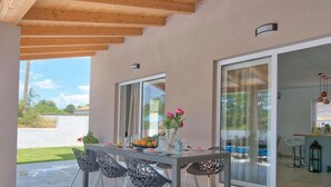 Un espace de restauration en plein air avec une table dressée pour quatre personnes, entourée de chaises, et une vue sur le jardin et le ciel.