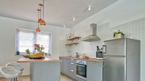 Une cuisine moderne dotée d’un îlot central, d’appareils électroménagers en acier inoxydable et de luminaires suspendus.