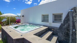A modern outdoor hot tub area with a stone wall and steps leading up to it, surrounded by a white building with windows and a clear blue sky. - Holiday Home in Playa Blanca (Yaiza)