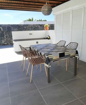 An outdoor patio with a table and chairs, a grill, and a stone wall in the background. - Holiday Home in Playa Blanca (Yaiza)