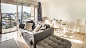 Ein modernes Wohnzimmer mit grauem Sofa, einem Esstisch mit Stühlen und einem Balkon mit Blick auf die Stadt.