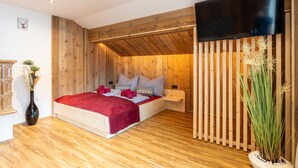 A bedroom with a wooden ceiling, a bed with red bedding, a TV, and a potted plant. - Comfortable Apartment in Salzburger Land (Neukirchen am Grossvenediger)