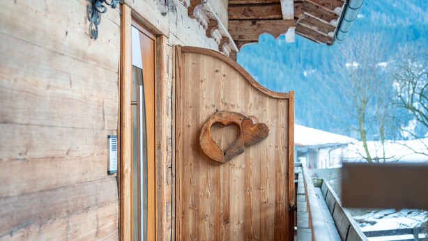 A wooden door with a heart-shaped decoration, a wooden exterior wall, and a snowy mountain background. - Comfortable Apartment in Salzburger Land (Neukirchen am Grossvenediger)