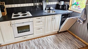 A compact kitchen with white cabinets, a black countertop, a stove, a sink, and a dishwasher. - 4 Person Holiday Home in Karlskoga (Karlskoga)
