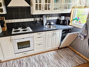 A compact kitchen with white cabinets, a black countertop, a stove, a sink, and a dishwasher. - 4 Person Holiday Home in Karlskoga (Karlskoga)