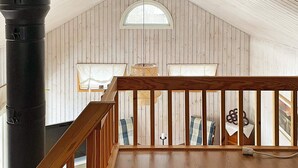 A loft-style room with a sloped ceiling, wooden walls, a wooden railing, and a large black pipe. - 4 Person Holiday Home in Karlskoga (Karlskoga)