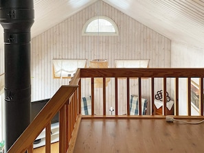 A loft-style room with a sloped ceiling, wooden walls, a wooden railing, and a large black pipe. - 4 Person Holiday Home in Karlskoga (Karlskoga)