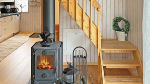 A cozy kitchen with a wood-burning stove, wooden staircase, and a potted plant. - 4 Person Holiday Home in Karlskoga (Karlskoga)