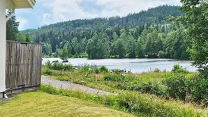 A lakeside property with a wooden deck, a grassy lawn, and a view of a forested hill. - 4 Person Holiday Home in Karlskoga (Karlskoga)