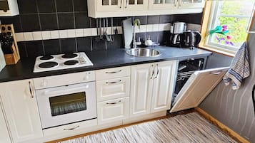 A compact kitchen with white cabinets, a black countertop, a stove, a sink, and a dishwasher.