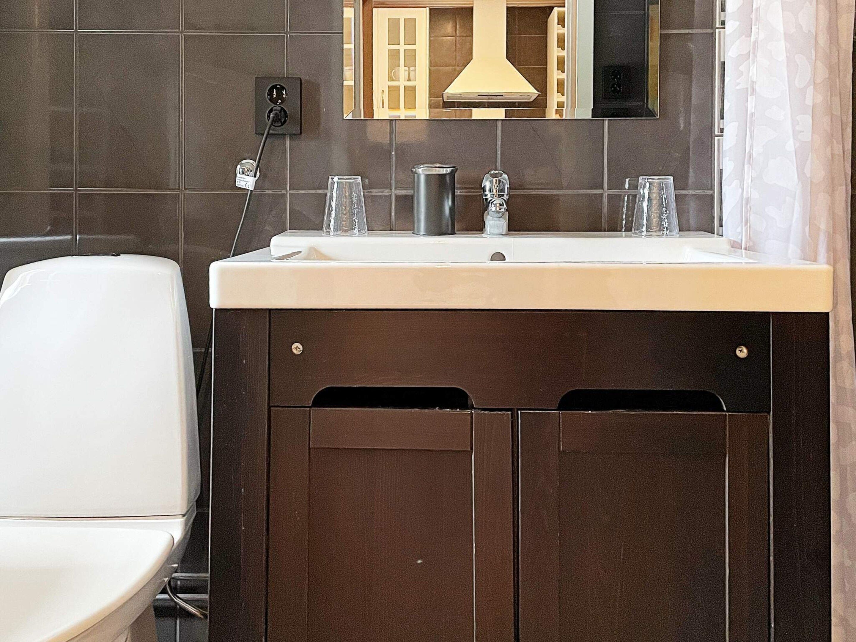 Een badkamer met een wit toilet, een wastafel met een spiegel erboven en een donker houten kast eronder.