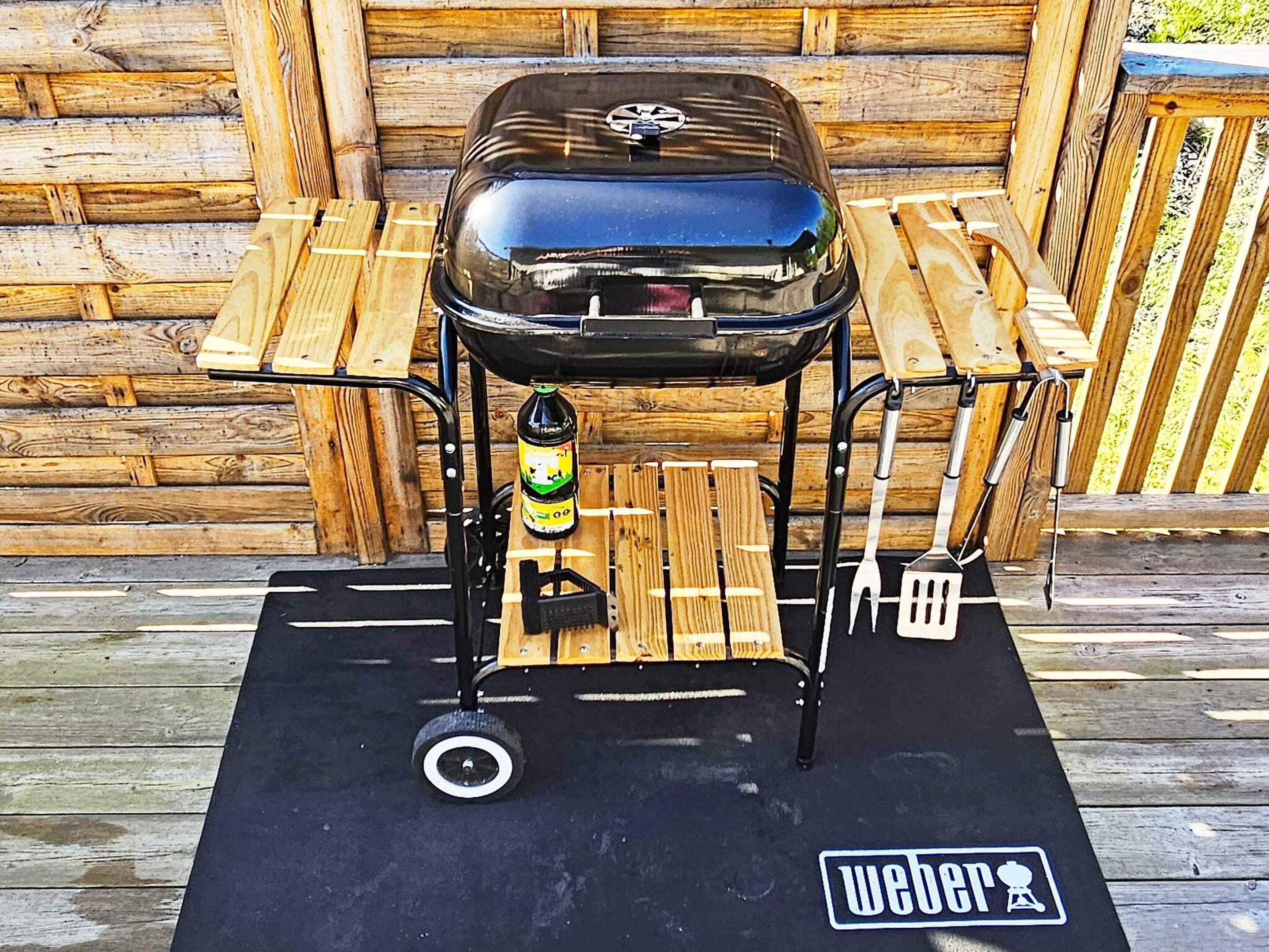 A portable barbecue grill with a bottle of beer on a mat with a logo.
