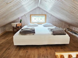 A cozy attic bedroom with a large bed, wooden walls, a small table with a plant, and a window.