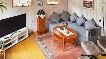 Ett vardagsrum med en platt-TV, en soffa, ett soffbord och en mönstrad matta.