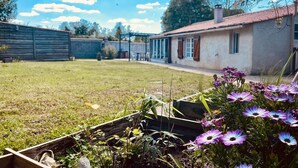 Un jardí amb una banca de fusta, una casa de maó i un cel blau clar.