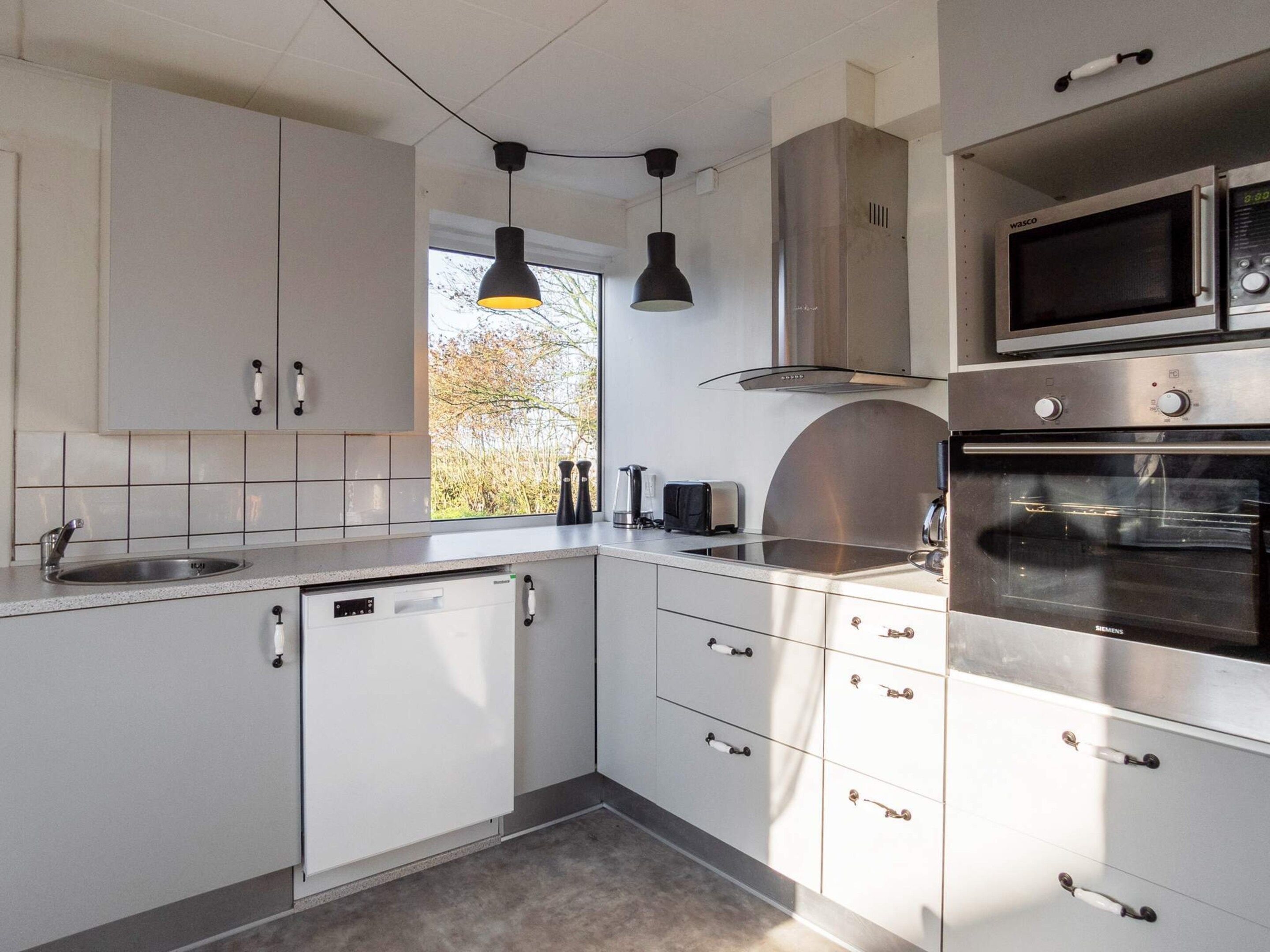 Una cocina moderna con gabinetes blancos, electrodomésticos de acero inoxidable e iluminación colgante.
