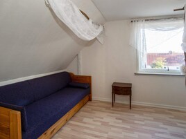 Una habitación con un banco de madera, una mesita de madera, un ventanal con cortinas blancas y un suelo con estampado de espiga.