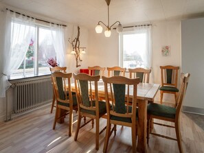A dining area with a wooden table and chairs, a radiator, and windows with curtains. - 8 Person Holiday Home in Lemvig-by Traum (Lemvig)