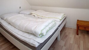 A single bed with white bedding and a wooden headboard in a room with wooden flooring and white walls.