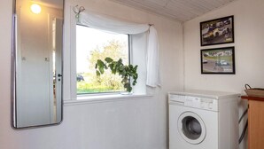 A laundry room with a washing machine, a window with curtains, and a mirror.