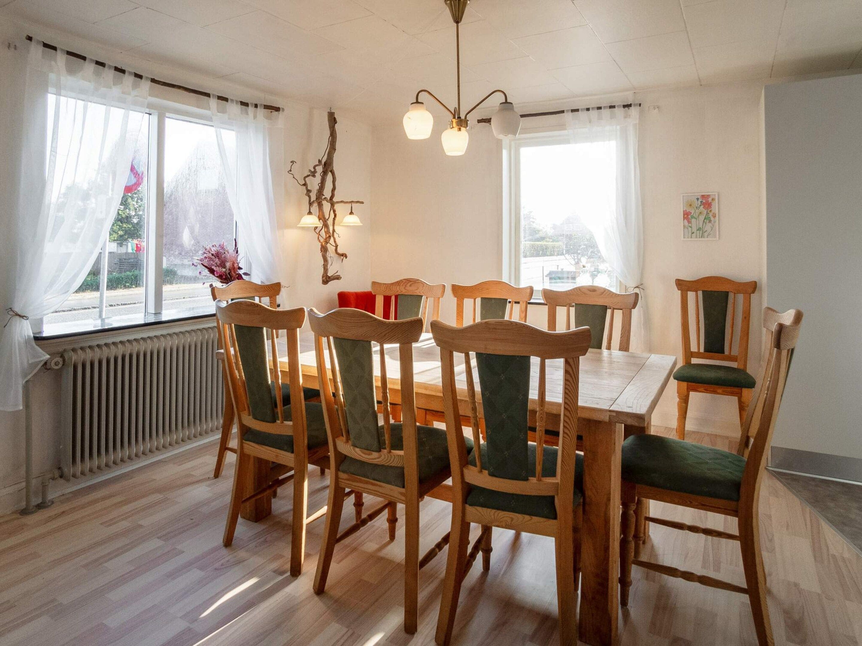 Ein Essbereich mit Holztisch und Stühlen, einem Heizkörper und einem Fenster mit Vorhängen.