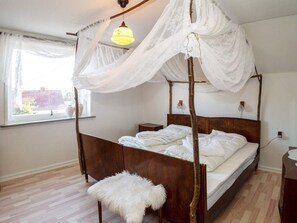 Ein Schlafzimmer mit Himmelbett, Baldachin, Nachttisch, Lampe und Fenster mit Blick nach draußen.