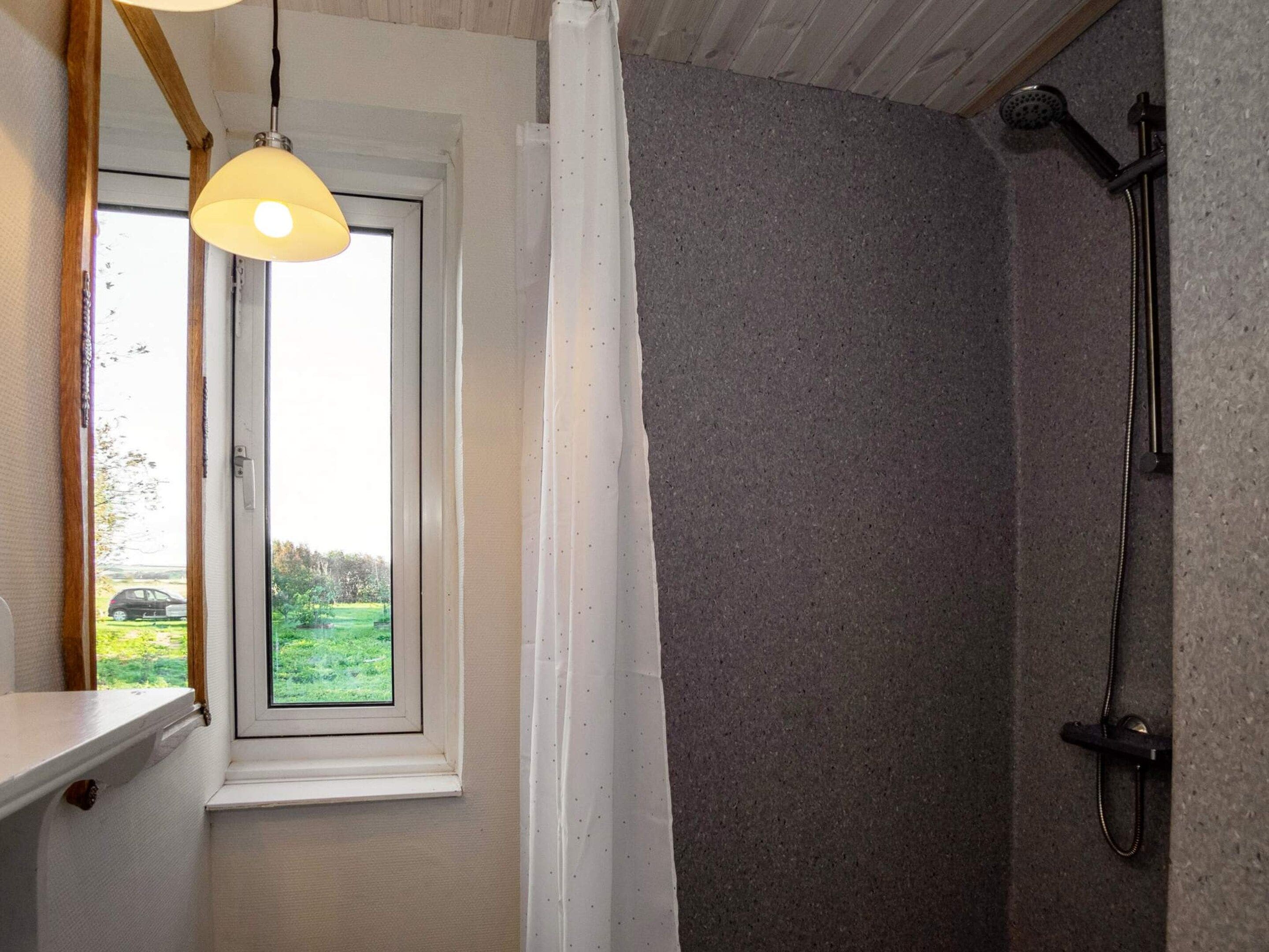 Casa de banho com chuveiro, janela com vista para vegetação e luminária suspensa.