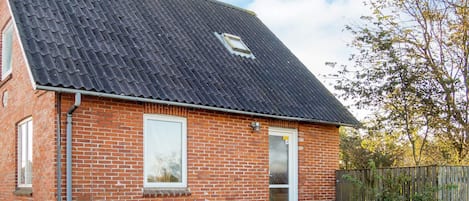 A brick house with a dark tiled roof, a wooden fence, and a clear sky.