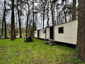 Een stacaravan met een terras, een tafel en stoelen.