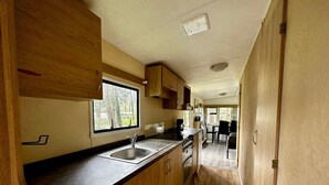 Cocina compacta con armarios de madera, un lavamanos y ventana con vistas a un jardín.