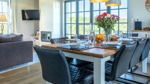 A modern dining area with a wooden table, black leather chairs, and pendant lighting. - Lush Villa With Sauna and Fireplace (Dranske)