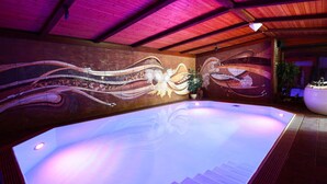 Une grande piscine intérieure avec une fresque murale, un escalier menant à un niveau supérieur et un plafond avec des poutres en bois.