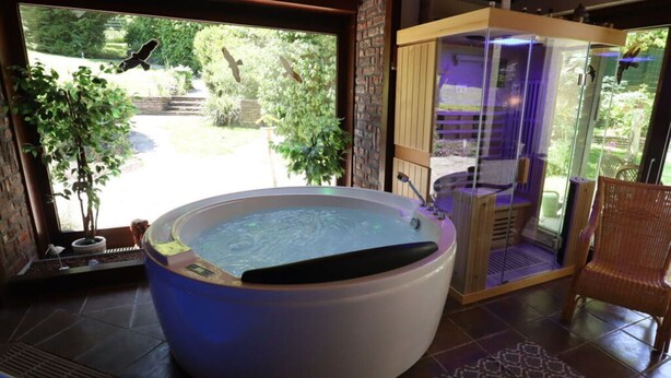 Un bain à remous dans une pièce donnant sur un jardin, le tout entouré de parois vitrées.