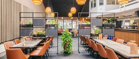 A modern restaurant with high tables, orange chairs, and hanging wicker lamps.