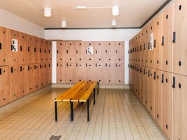 A locker room with multiple wooden lockers, a wooden bench, and a tiled floor.