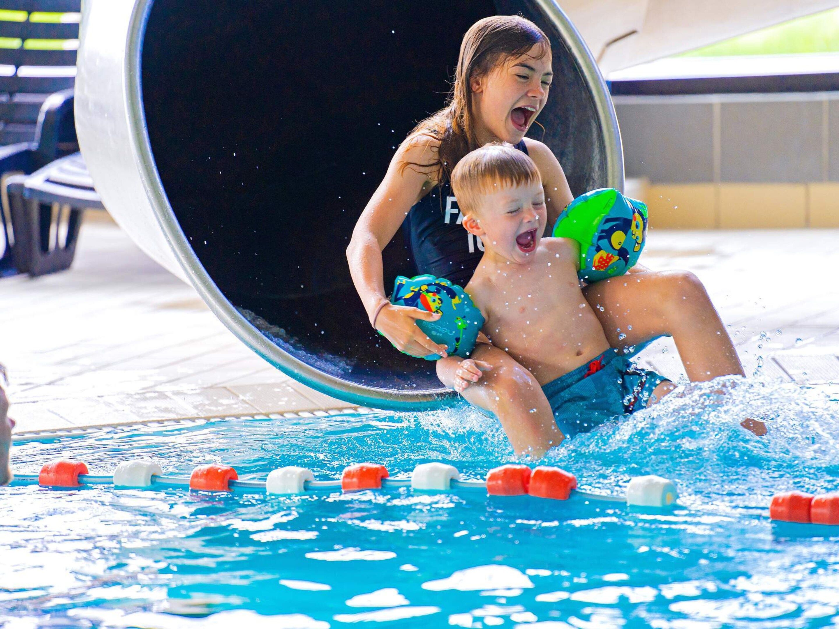 A pool with a water slide, lane markers, and a person and child in the water.