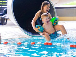 Una piscina con tobogán acuático, marcas de carril y una persona y un niño en el agua.