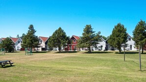 A grassy area with a picnic table, trees, and a row of buildings with red roofs. - 6 Person Holiday Park Home in Blavand (Blavand)