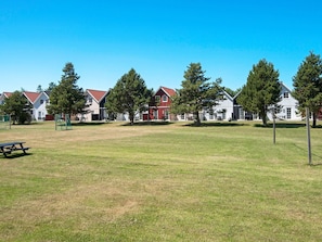 A grassy area with a picnic table, trees, and a row of buildings with red roofs. - 6 Person Holiday Park Home in Blavand (Blavand)