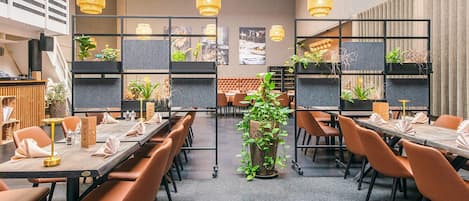 Un'area pranzo moderna con tavoli lunghi, sedie marroni e lampade in vimini pendenti.