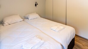 A bedroom with two beds, white bedding, a wooden floor, and a sliding door closet. - House With a Terrace on the Edge of the Forest (Baars)