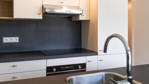 A modern kitchen with white cabinets, a stainless steel range hood, a built-in dishwasher, and a stainless steel sink. - House With a Terrace on the Edge of the Forest (Baars)