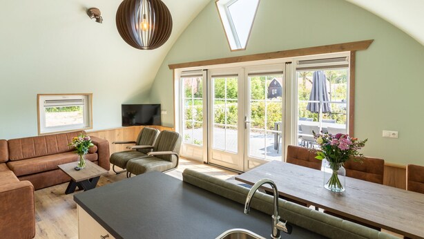 A modern kitchen with a large island, built-in appliances, and a dining area with a view of the garden. - House With a Terrace on the Edge of the Forest (Baars)