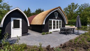 A building with two distinct sections, one with a white door and another with a large window, both featuring a thatched roof. - House With a Terrace on the Edge of the Forest (Baars)