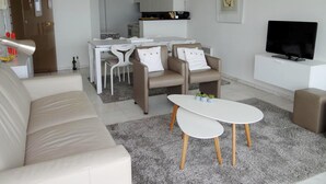 A modern living room with a sofa, two armchairs, a coffee table, a TV, and a dining area with a table and chairs. - Apartment in Nieuwpoort With Terrace (Nieuwpoort)