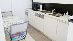 A compact kitchen with white cabinets, a coffee maker, a sink, and a small table with a chair. - Apartment in Nieuwpoort With Terrace (Nieuwpoort)