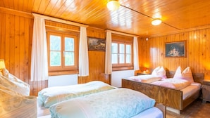A wooden cabin room with two beds, a painting on the wall, and a window with curtains.