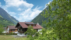 A chalet-style house with a sloped roof, wooden balconies, and a view of a mountainous landscape.