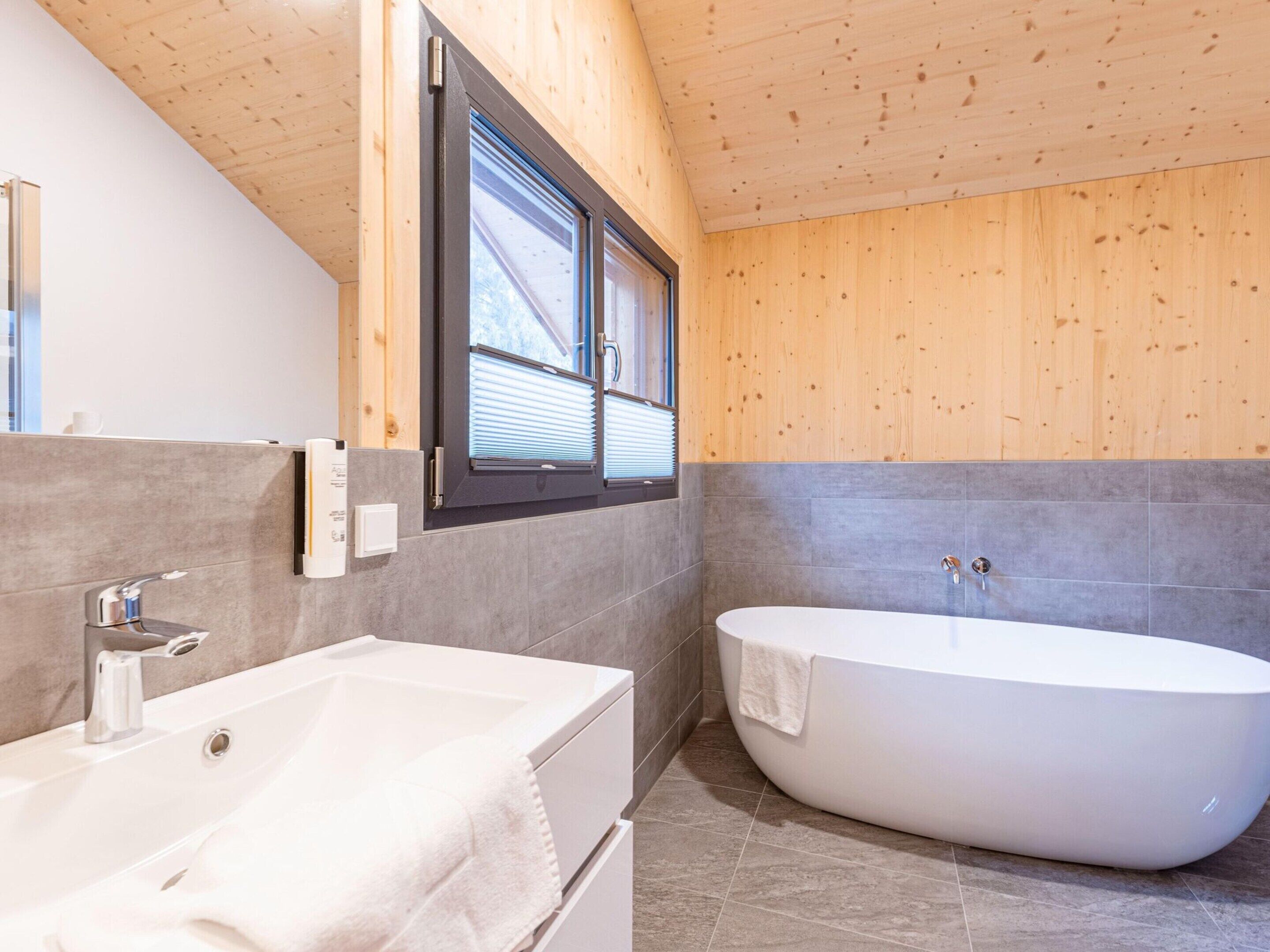 Une salle de bain moderne avec une baignoire sur pieds, un grand miroir et un lambris en bois sur les murs.