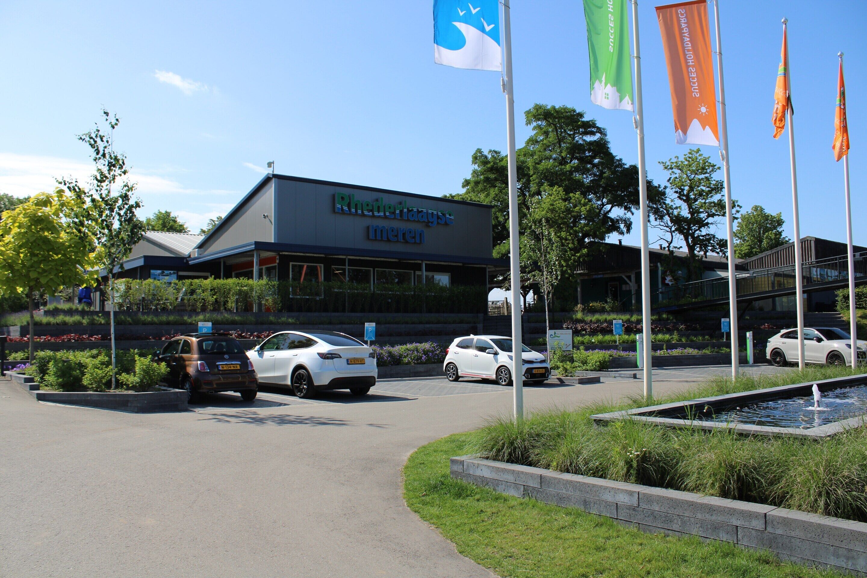 Un bâtiment avec une enseigne indiquant « Rhederhaagtenmeren » et un parking où sont garées plusieurs voitures.
